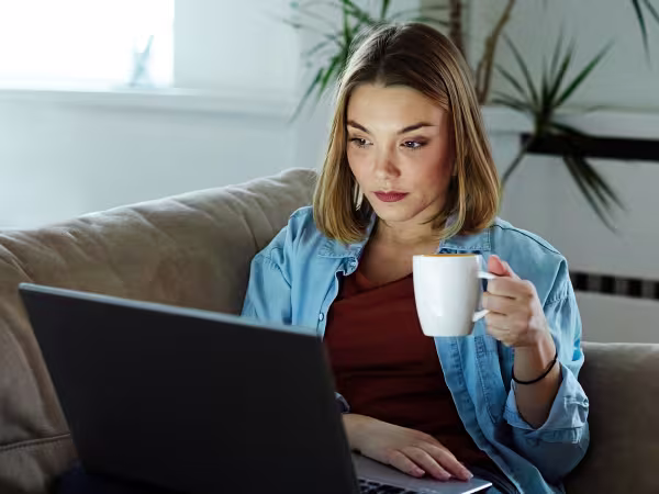 Focused woman holding a cup and looking at her laptop screen