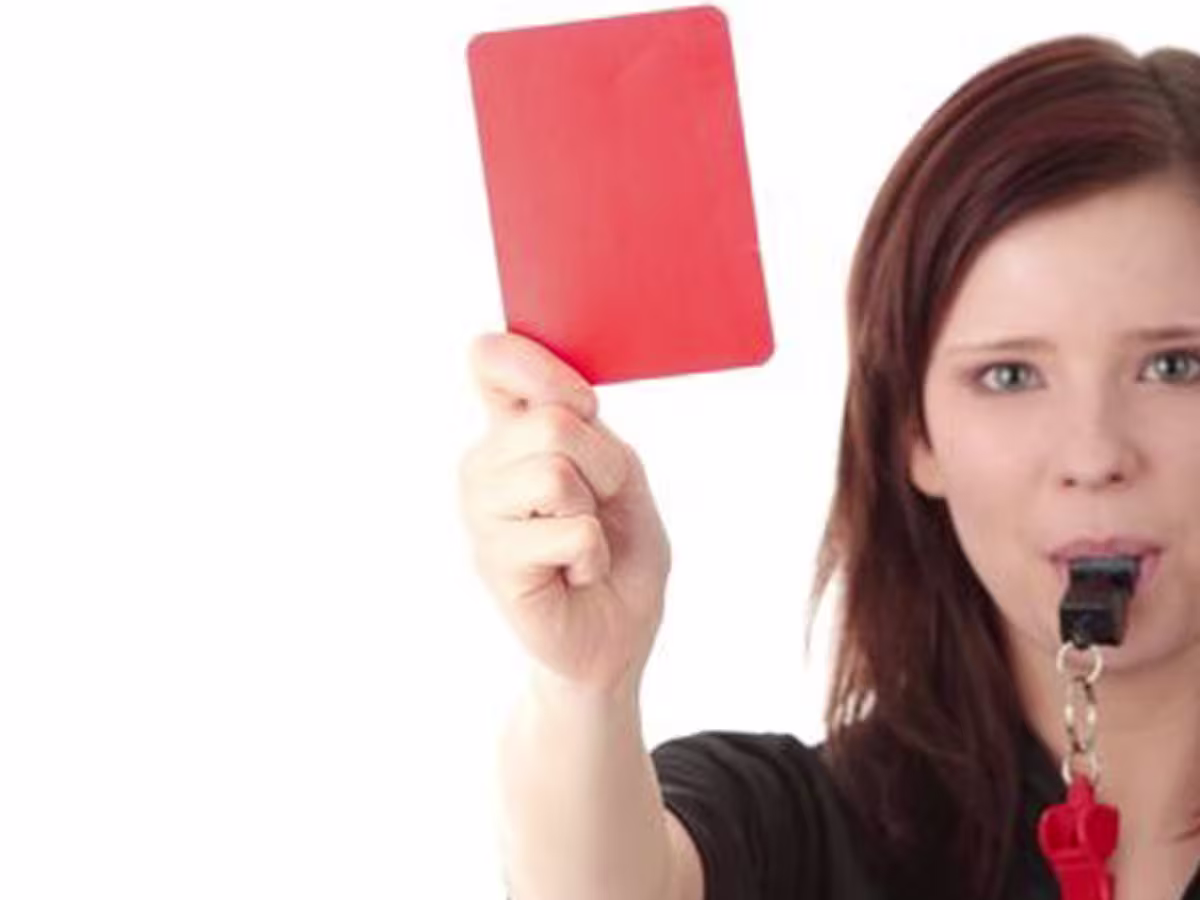 Female referrer blowing whistle holding red card